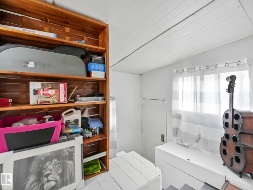 This room features a wooden shelving unit, a window with sheer white curtains, and white planked walls and ceiling - 12141 96 Street, Edmonton, AB - Indoor Photo Showing Other Room