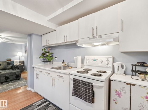 The property features a kitchen with white cabinetry, a sink, and a white electric range with an overhead range hood - 12141 96 Street, Edmonton, AB - Indoor Photo Showing Kitchen