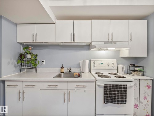 The kitchen features white cabinetry with brushed nickel hardware, a stainless steel sink, and a white electric range with an overhead range hood - 12141 96 Street, Edmonton, AB - Indoor Photo Showing Kitchen
