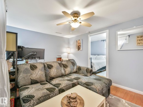 This living area features light-colored walls, a ceiling fan with integrated lighting, and wood flooring - 12141 96 Street, Edmonton, AB - Indoor