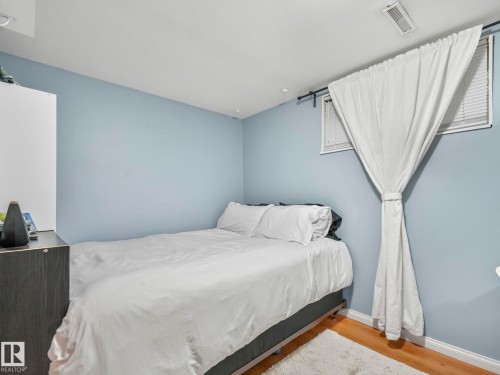 This room features light blue walls, hardwood flooring, and a window with white blinds and curtains - 12141 96 Street, Edmonton, AB - Indoor Photo Showing Bedroom