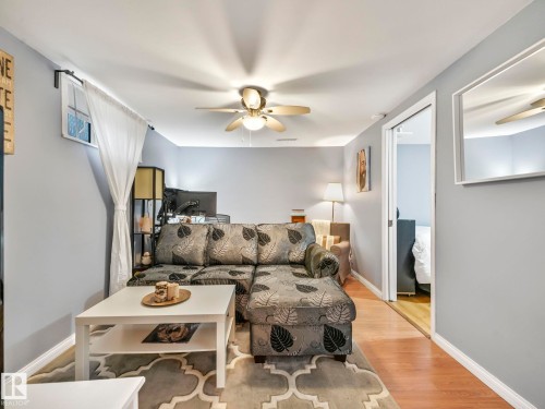 Living area featuring light gray walls, hardwood flooring, a ceiling fan with integrated lighting, and a doorway opening to an additional room - 12141 96 Street, Edmonton, AB - Indoor