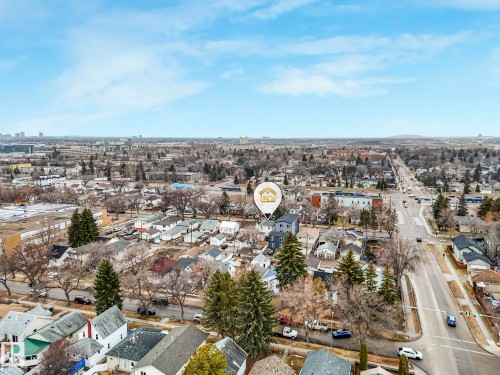 Aerial view highlighting the property's location within a residential neighborhood featuring mature trees, a clear main road, and a distant city skyline - 12141 96 Street, Edmonton, AB - Outdoor With View