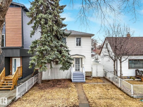 The property features a white exterior, a front porch with light blue railings, and a mature tree in the front yard - 12141 96 Street, Edmonton, AB - Outdoor