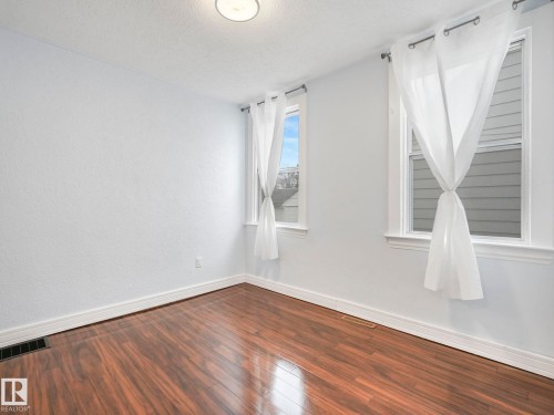This room features sleek wood flooring, light-colored walls, and two windows - 12141 96 Street, Edmonton, AB - Indoor Photo Showing Other Room