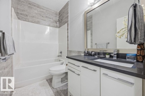 Bathroom featuring a white bathtub and shower with textured gray wall tiling, a vanity with a dark countertop, an integrated sink, and a large mirror - 17534 60A Street, Edmonton, AB - Indoor Photo Showing Bathroom