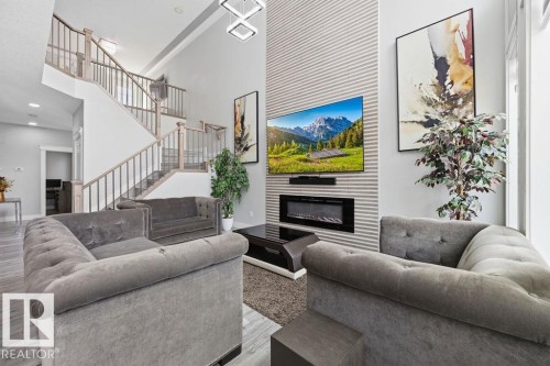 Living area featuring high ceilings, a prominent staircase with light wood railings, and an entertainment wall with a mounted television and a sleek fireplace - 17534 60A Street, Edmonton, AB - Indoor Photo Showing Living Room With Fireplace