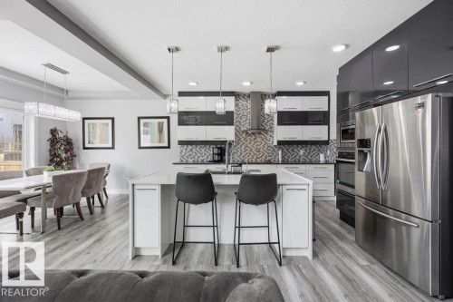 The kitchen features a large island with seating, stainless steel appliances, and a mosaic tile backsplash - 17534 60A Street, Edmonton, AB - Indoor Photo Showing Kitchen With Stainless Steel Kitchen With Upgraded Kitchen