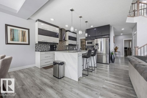 The property features a kitchen with a central island, stainless steel appliances, and sleek cabinetry, complemented by light wood-style flooring throughout - 17534 60A Street, Edmonton, AB - Indoor Photo Showing Kitchen With Upgraded Kitchen