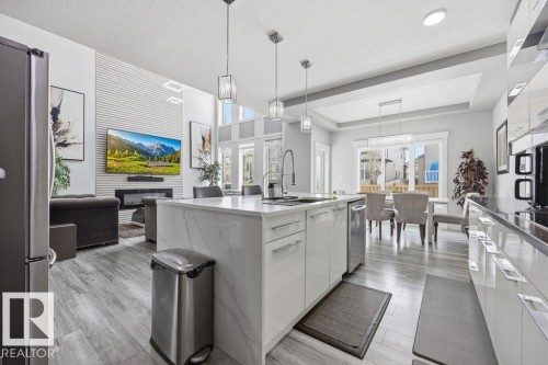 This open-concept living space features light-toned flooring, a kitchen island with a sink and pendant lighting, and a dining area with large windows - 17534 60A Street, Edmonton, AB - Indoor Photo Showing Kitchen With Upgraded Kitchen