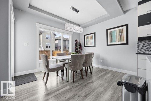 The dining area features engineered hardwood flooring, a modern linear chandelier, and a large window providing natural light - 17534 60A Street, Edmonton, AB - Indoor Photo Showing Dining Room
