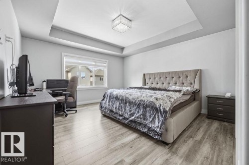 This room features a tray ceiling with a contemporary light fixture, a window providing natural light, and light-toned flooring - 17534 60A Street, Edmonton, AB - Indoor Photo Showing Bedroom