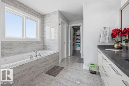 The bathroom features a built-in bathtub with a window, tile flooring, and a vanity with a dark countertop and white cabinetry - 17534 60A Street, Edmonton, AB - Indoor Photo Showing Bathroom