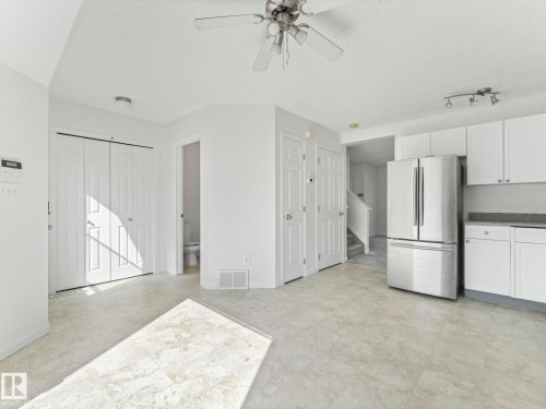 Open concept living area featuring tiled flooring, a ceiling fan, and a kitchen with white cabinetry and a stainless steel refrigerator - 675 Mcallister Loop, Edmonton, AB - Indoor Photo Showing Kitchen
