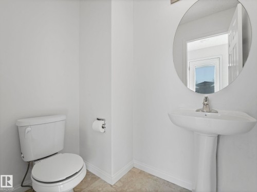 Bathroom featuring a pedestal sink with a chrome faucet, a round wall-mounted mirror, and neutral-toned flooring - 675 Mcallister Loop, Edmonton, AB - Indoor Photo Showing Bathroom