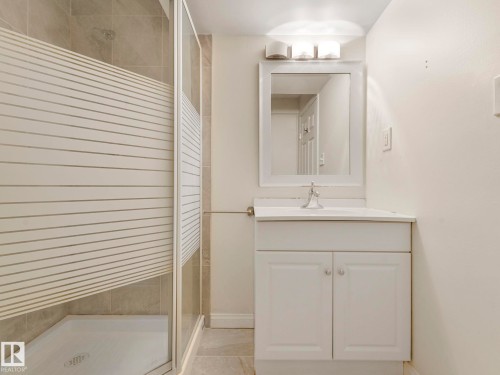 Bathroom featuring a white vanity with an integrated sink, a framed mirror, and a shower with a frosted glass enclosure - 675 Mcallister Loop, Edmonton, AB - Indoor Photo Showing Bathroom