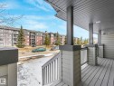 The property features a private balcony with plank flooring, sturdy pillars, and a railing, offering views of the surrounding apartment buildings and trees - 675 Mcallister Loop, Edmonton, AB  - Outdoor With Deck Patio Veranda With Exterior 