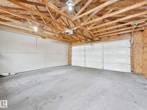 Spacious garage with exposed wooden beams, a concrete floor, and two white garage doors - 675 Mcallister Loop, Edmonton, AB - Indoor Photo Showing Garage