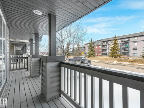 The property features a covered porch with a wooden deck and railings, offering views of the street and nearby buildings - 675 Mcallister Loop, Edmonton, AB - Outdoor With Deck Patio Veranda With Exterior