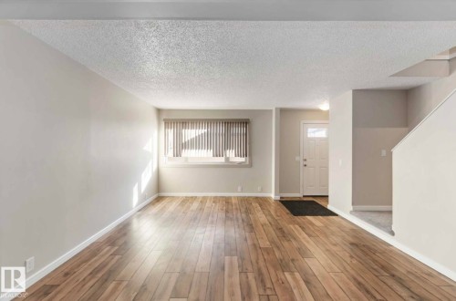 The living space features hardwood flooring, a window with blinds, and a white front door with a window pane - 8 14511 52 Street, Edmonton, AB - Indoor Photo Showing Other Room