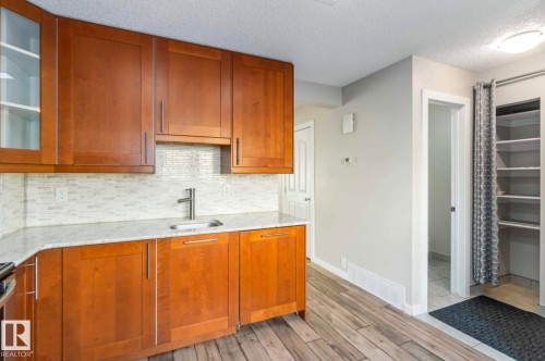 This kitchen features wooden cabinetry with a light-colored countertop and a white tiled backsplash - 8 14511 52 Street, Edmonton, AB - Indoor Photo Showing Kitchen