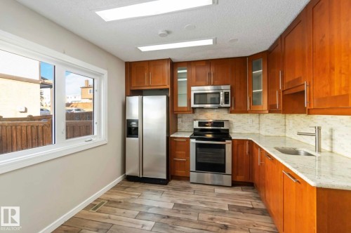 The kitchen features wood cabinetry, stainless steel appliances, a tile backsplash, and a sink with a modern faucet - 8 14511 52 Street, Edmonton, AB - Indoor Photo Showing Kitchen