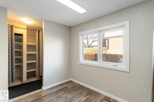 This room features wood-look flooring, a window providing natural light, and a closet with shelving and privacy curtains - 8 14511 52 Street, Edmonton, AB - Indoor Photo Showing Other Room