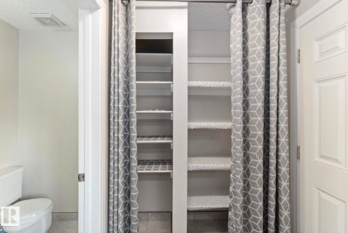 This area features built-in shelving with shelf liners, enclosed by decorative curtains on a curtain rod - 8 14511 52 Street, Edmonton, AB - Indoor Photo Showing Bathroom
