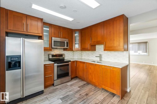 The kitchen features wood cabinetry, stainless steel appliances, and light-colored countertops with a tiled backsplash - 8 14511 52 Street, Edmonton, AB - Indoor Photo Showing Kitchen