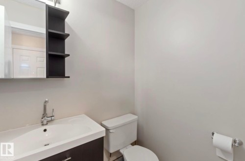 Bathroom featuring a vanity with an integrated sink and chrome faucet, a wall-mounted mirror, and a toilet - 8 14511 52 Street, Edmonton, AB - Indoor Photo Showing Bathroom