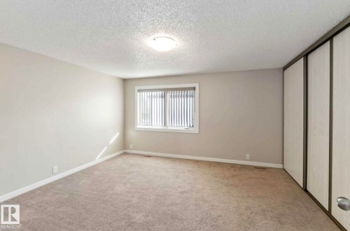 This room features neutral-toned carpet, light gray walls, and a window with vertical blinds - 8 14511 52 Street, Edmonton, AB - Indoor Photo Showing Other Room