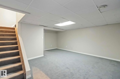 Expansive room featuring light gray carpeting and white baseboards, with a drop ceiling and an overhead light fixture - 8 14511 52 Street, Edmonton, AB - Indoor