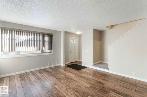 The property features hardwood flooring, light-colored walls, and a window with blinds providing natural illumination - 8 14511 52 Street, Edmonton, AB - Indoor Photo Showing Other Room