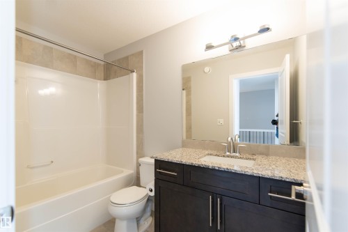 Bathroom featuring a white bathtub with a tiled surround, a toilet, and a vanity with a granite countertop and a white undermount sink - 1793 Keene Crescent, Edmonton, AB - Indoor Photo Showing Bathroom