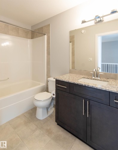 Bathroom with light-colored tile flooring, a white bathtub, and a dark wood vanity with a light granite countertop - 1793 Keene Crescent, Edmonton, AB - Indoor Photo Showing Bathroom