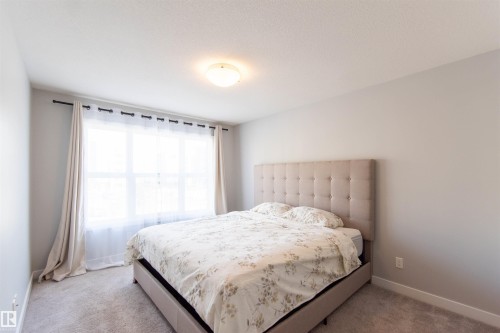 This room features a large window with drapes, a light-colored upholstered bed frame, and carpeted flooring - 1793 Keene Crescent, Edmonton, AB - Indoor Photo Showing Bedroom