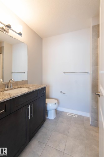 Bathroom featuring a dark wood vanity with a granite countertop and an undermount sink, a toilet, and light-colored tiled flooring - 1793 Keene Crescent, Edmonton, AB - Indoor Photo Showing Bathroom