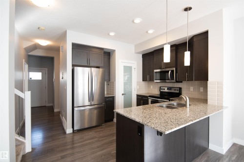 The kitchen features dark cabinetry, stainless steel appliances, a granite countertop, and pendant lighting over the island - 1793 Keene Crescent, Edmonton, AB - Indoor Photo Showing Kitchen With Double Sink With Upgraded Kitchen
