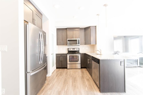 Kitchen featuring stainless steel appliances, dark wood cabinetry, light-colored countertops, and light wood-style flooring - 1793 Keene Crescent, Edmonton, AB - Indoor Photo Showing Kitchen With Upgraded Kitchen