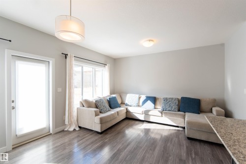 Living area featuring grey walls, dark wood-style flooring, a large window with white curtains, and a glass-paneled door - 1793 Keene Crescent, Edmonton, AB - Indoor Photo Showing Living Room
