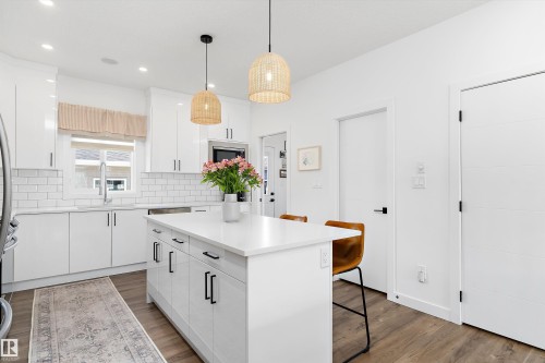 The kitchen features a large island with a white countertop and seating for two, white cabinetry with black hardware, and wood flooring - 1305 Enright Landing, Edmonton, AB - Indoor Photo Showing Kitchen With Upgraded Kitchen