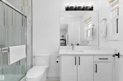 The bathroom features a modern vanity with a white countertop and dark-colored pulls, a large mirror, and an enclosed shower with a glass door - 1305 Enright Landing, Edmonton, AB - Indoor Photo Showing Bathroom