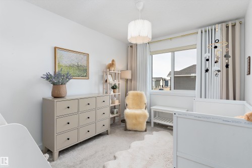 This bright room features a window with blinds and curtains, a light-colored carpet, and a decorative ceiling light fixture - 1305 Enright Landing, Edmonton, AB - Indoor Photo Showing Bedroom