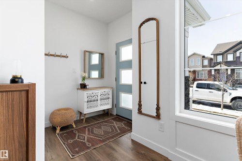 The entryway features wood flooring, a light blue front door with frosted glass panels, and a large window providing views of the neighborhood - 1305 Enright Landing, Edmonton, AB - Indoor Photo Showing Other Room