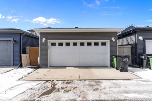 Detached garage with a white panel door featuring rectangular window inserts, grey horizontal siding, and two exterior wall sconces - 1305 Enright Landing, Edmonton, AB - Outdoor With Exterior