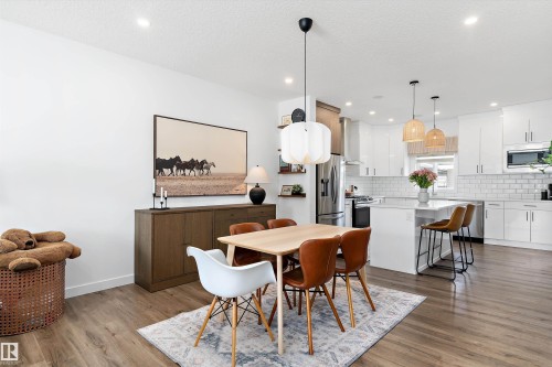 The open-concept living space features hardwood floors, a dining area with a modern chandelier, and a kitchen with white cabinetry and an island with bar seating - 1305 Enright Landing, Edmonton, AB - Indoor