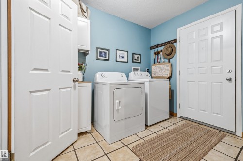 The property features a laundry area with tile flooring, a washer and dryer, and wall-mounted cabinetry - 17 Sunset Harbour, Rural Wetaskiwin County, AB - Indoor Photo Showing Laundry Room