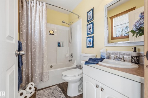 Bathroom featuring a white vanity with a built-in sink, a toilet, a bathtub with an overhead shower, and a decorative mirror - 17 Sunset Harbour, Rural Wetaskiwin County, AB - Indoor Photo Showing Bathroom
