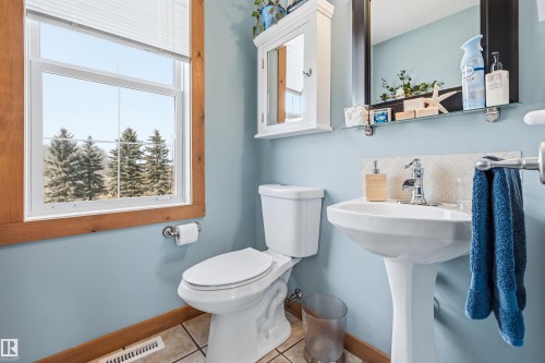 The bathroom features a pedestal sink with a chrome faucet, a toilet, and a window with wood trim - 17 Sunset Harbour, Rural Wetaskiwin County, AB - Indoor Photo Showing Bathroom