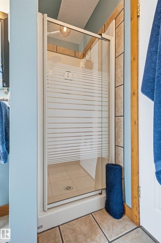 Bathroom featuring a glass-enclosed shower with a patterned privacy screen, tiled walls, and a tiled floor - 17 Sunset Harbour, Rural Wetaskiwin County, AB - Indoor